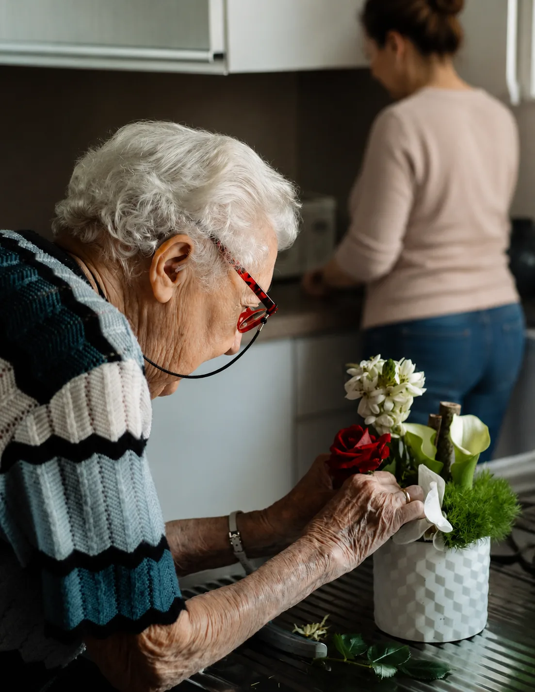 Seniorka układająca kwiaty w kuchni - opieka przy Parkinsonie